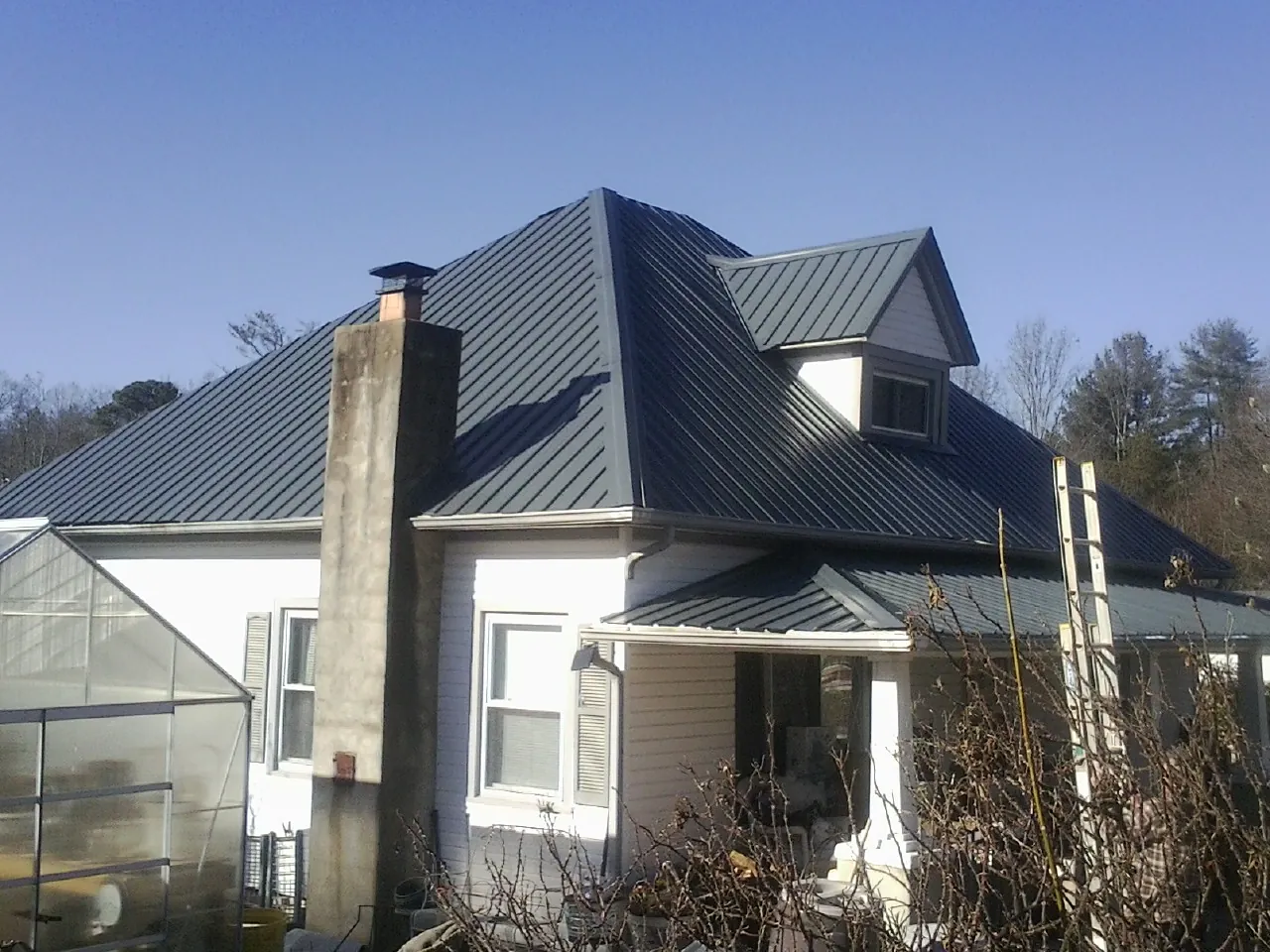 Dark blue standing seam metal roof on a white farmhouse with dormer — Slate & Tile Roof Repair by Roofing Brothers in Glenoma