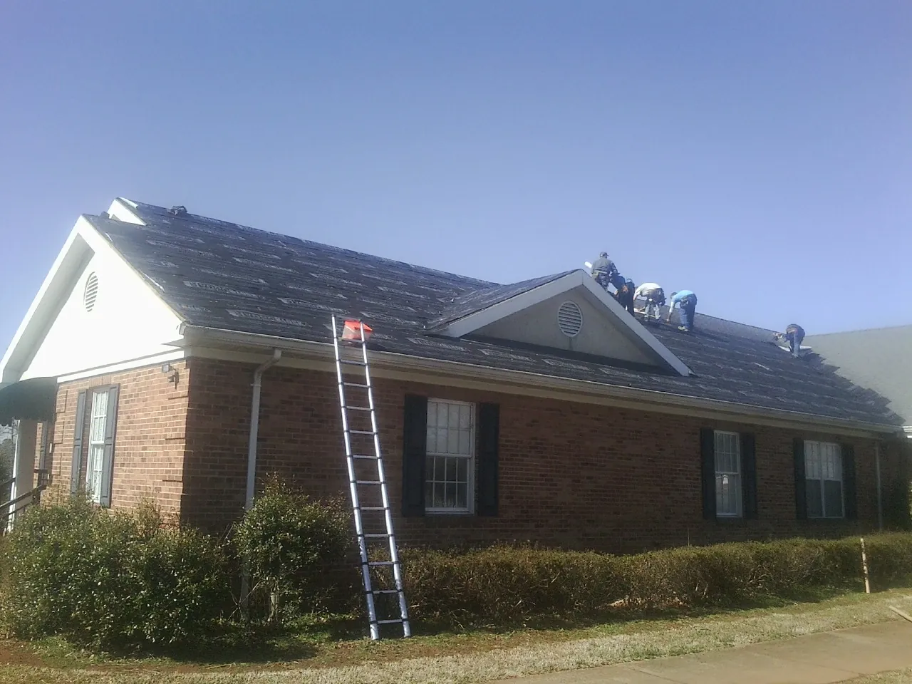 Crew tearing shingles off a brick ranch roof with a ladder set — Emergency Roof Repair work by our crew in Glenoma