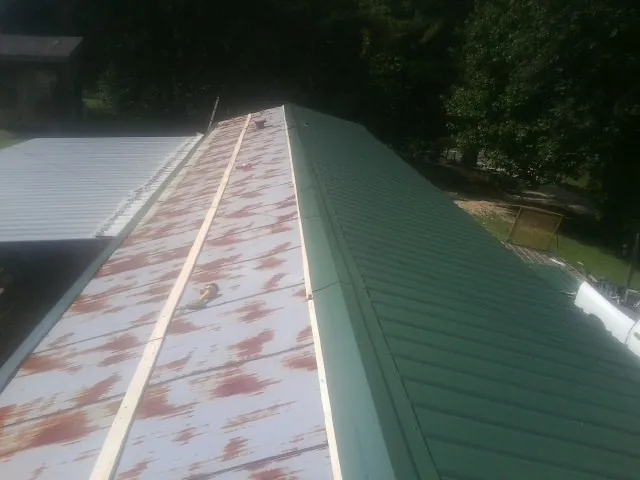 Old rusted panels beside newly installed green metal roofing — Wind Damage Roof Repair by Roofing Brothers in Glenoma