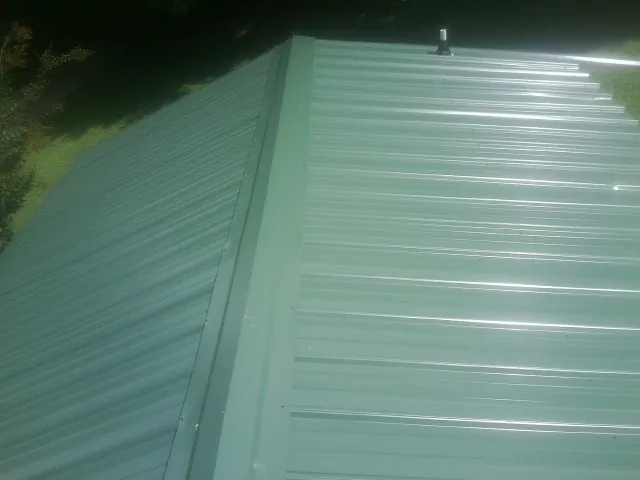 New green metal panels meeting at the ridge of a roof — Flat Roof Repair work by our crew in Glenoma