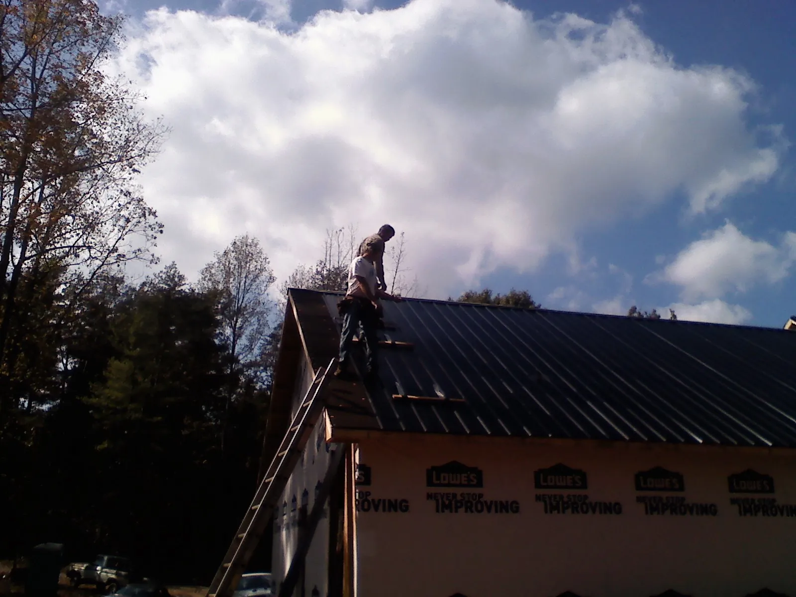 Roofer fastening dark metal panels high against a cloudy sky, from a Roof Inspection job in Glenoma
