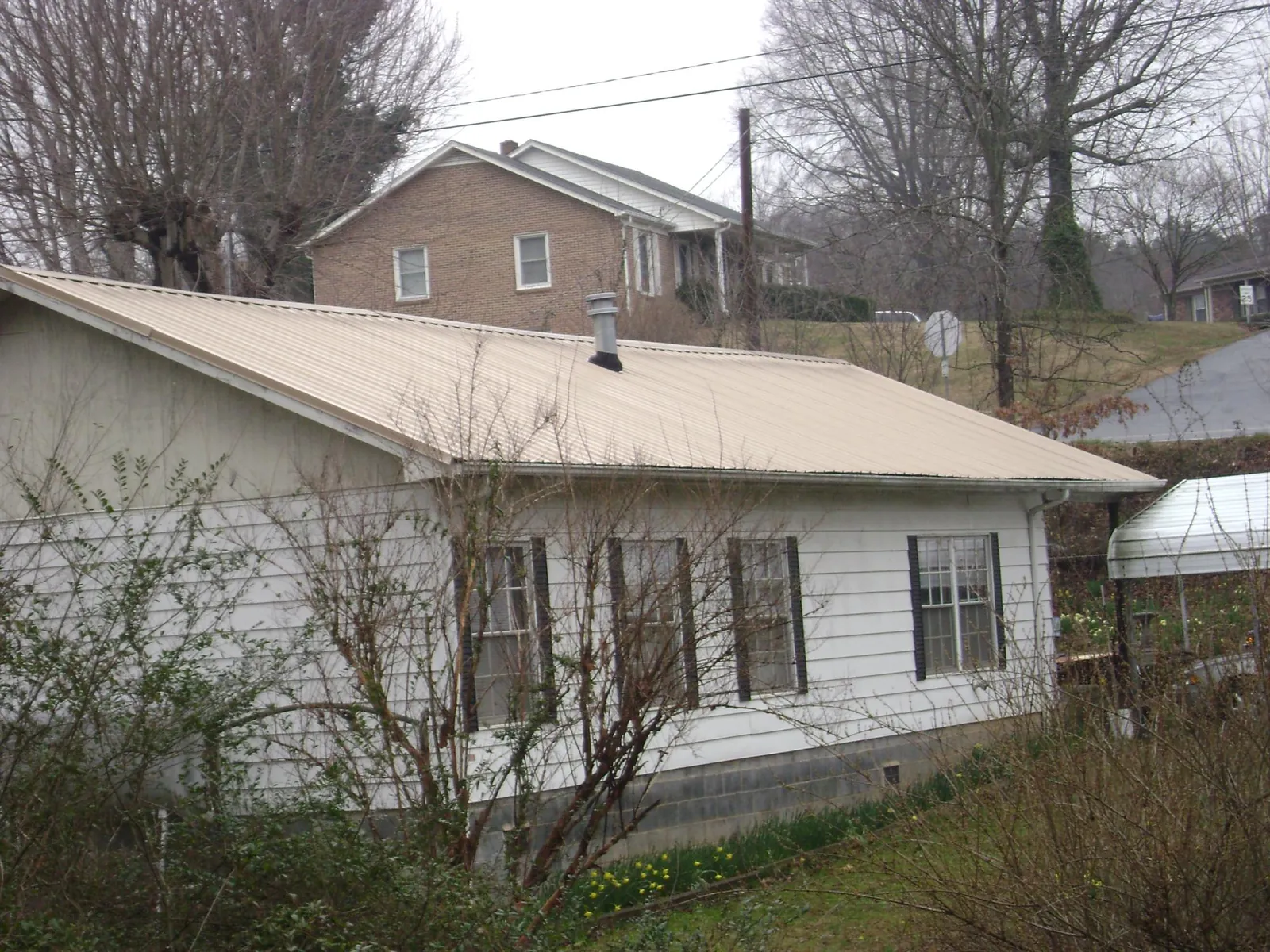 Tan metal roof on a white sided house set into a hillside — Commercial Roofing by Roofing Brothers in Glenoma